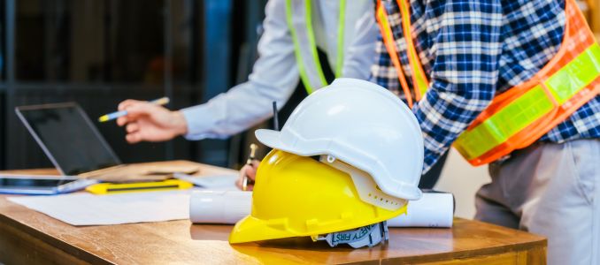 Construction team meeting with hard hats, laptop and blueprints on a desk, showing planning, safety and teamwork at a worksite