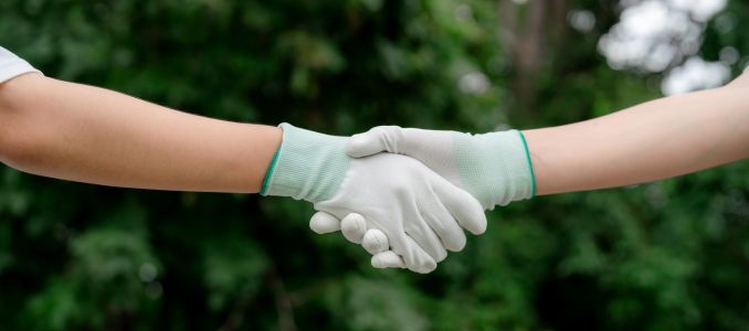 Two people wearing white protective work gloves shaking hands against green natural background