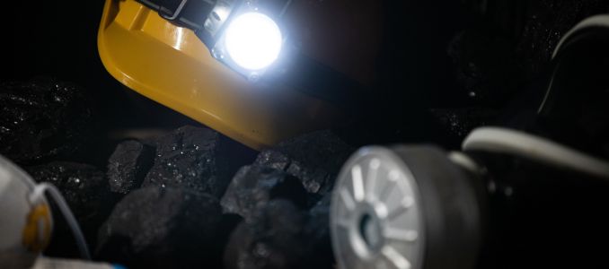 A protective helmet with a glowing flashlight and a dust mask with a filter lie on top of the black coal