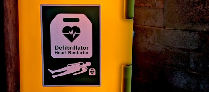 Automated External Defibrillator (AED) sign on a brightly illuminated yellow wall cabinet