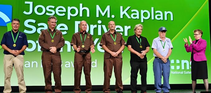 Six award recipients wearing medals stand on stage in front of a green backdrop for the Joseph M. Kaplan Safe Driver of the Year Award.