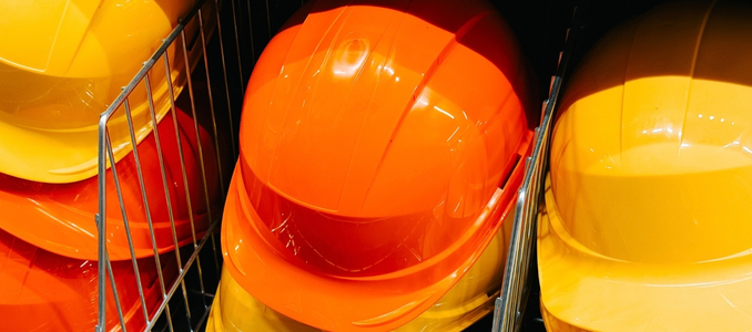 Bright orange and yellow construction hard hats stored side-by-side in wire rack bins.