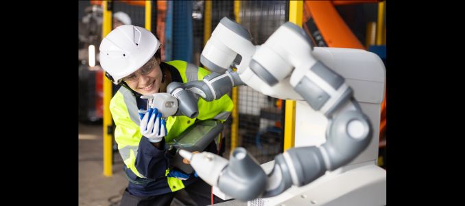 Worker inspects a robotic arm in an industrial facility.