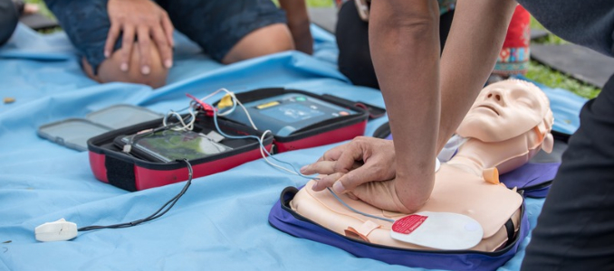 A close-up of a person practicing CPR compressions and AED pad placement on a training mannequin lying on a blue tarp.