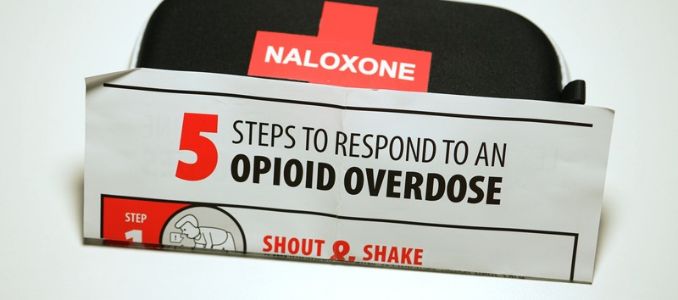 Naloxone kit behind a card outlining five steps to respond to an opioid overdose.