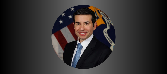 Official portrait of Keith Sonderling, U.S. Secretary of Labor, in a suit and blue tie in front of the U.S. Department of Labor seal and American flag.
