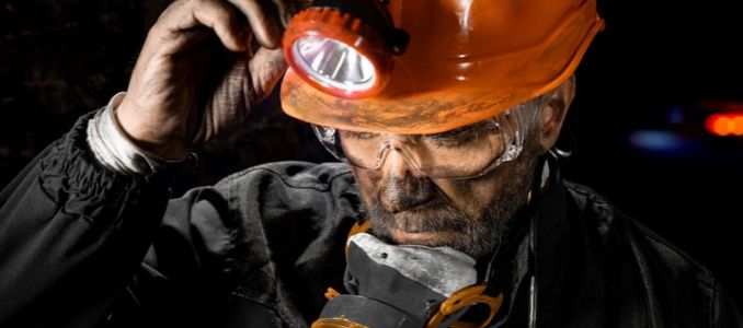 A miner wearing a headlamp, safety goggles, and a respirator.