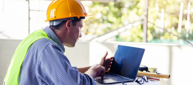 A site supervisor wearing a yellow hard hat and safety vest completing online training on a laptop at a job site.