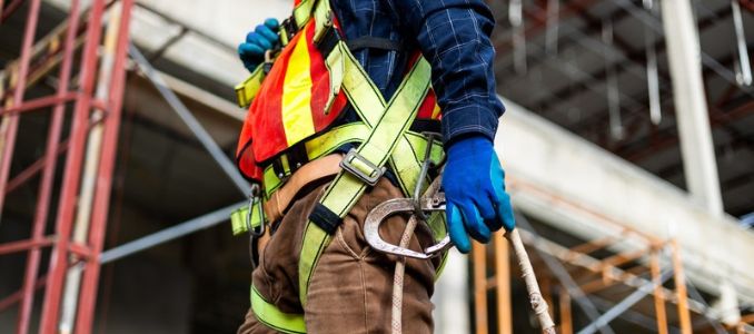 A construction worker wearing a safety harness, reflective vest and blue gloves.