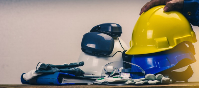 Personal protective equipment (PPE) laid out on a table, including yellow, blue, and white hard hats, earmuffs, safety glasses, and work gloves.