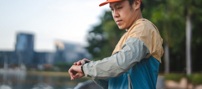 A man in athletic wear checking his smartwatch while standing outdoors near a park and city skyline.