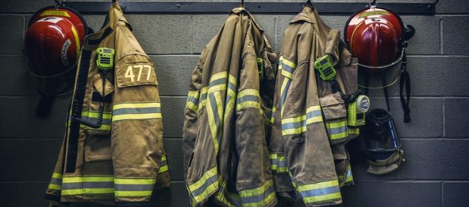 Firefighter turnout coats with reflective stripes, red helmets and radios hanging on hooks.