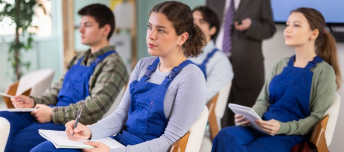 A group of trainees seated in a classroom taking notes during a training session.