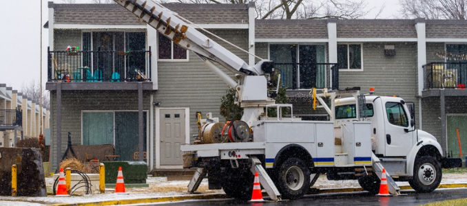 A utility derrick auger truck parked in front of a residential building during snowfall.