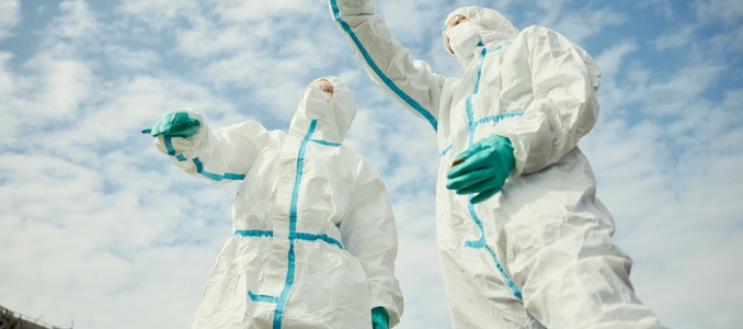 Two Asian young adult scientists wearing hazmat suits gesturing upward outdoors