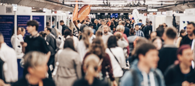 A crowded exhibition hall filled with attendees walking through trade show booths and displays.