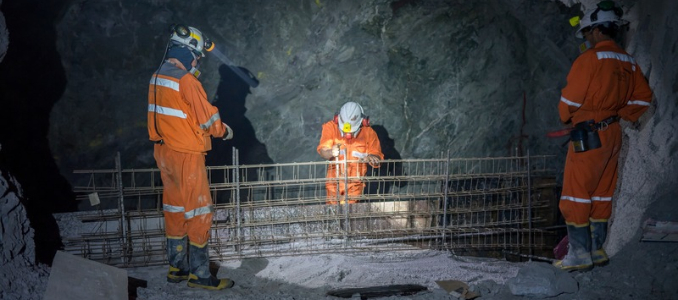 Three underground mine workers in orange protective gear working around steel reinforcement.
