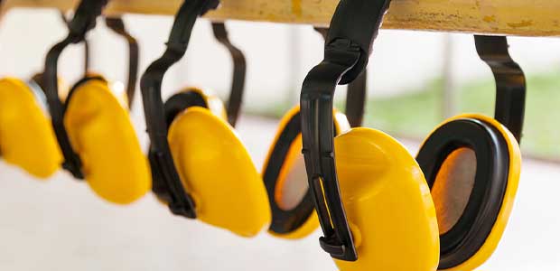 four yellow over-the-head earmuffs with black padding hanging on a yellow bar