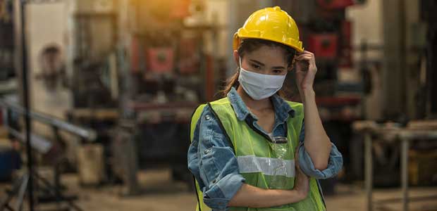 woman in vest, hard hat and face mask looking down in workplace confused