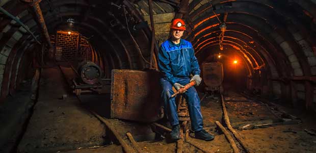 a coal miner stands in mine with tracks leading down two paths