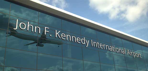 John F. Kennedy International Airport sign on glass building which reflects a landing plane