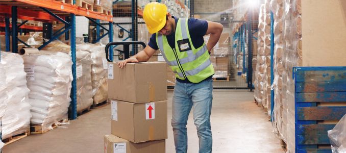 Factory worker experiencing back ache while moving boxes