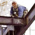 A picture of a construction worker welding together steel beams from high above the ground.