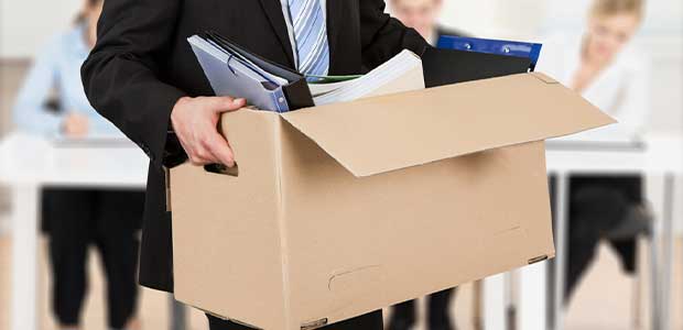 person wearing black suit and tie carrying a cardboard box filled with notebooks, binders and paper