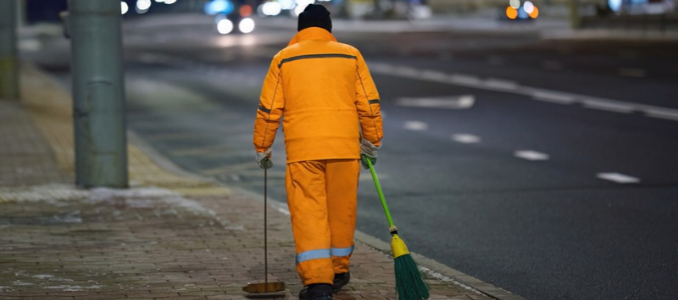 A sanitation worker sweeping a city sidewalk at night.