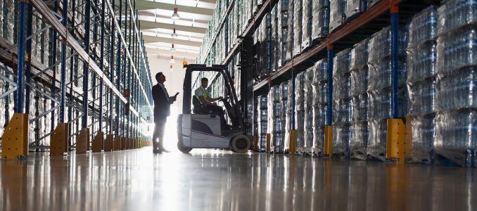 Male supervisor and worker operating forklift in distribution warehouse