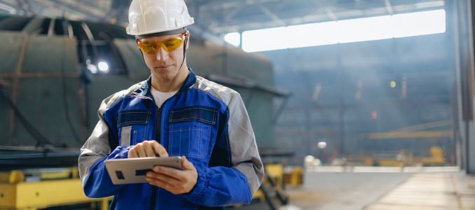Male engineer in shipyard wearing safety gear and using tablet in industrial setting