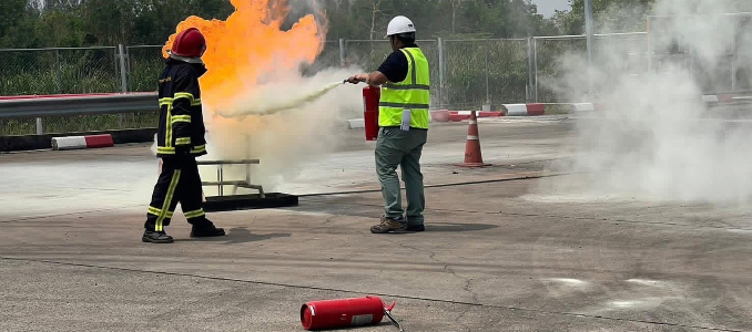 Workers conduct a fire safety training exercise using a fire extinguisher to control flames.