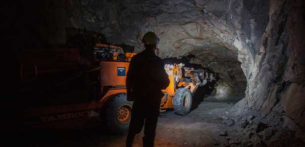 Miner standing in dark underground mine next to a drilling rig machine