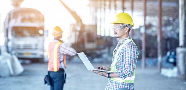 a person holding a computer stands in front of a trash truck
