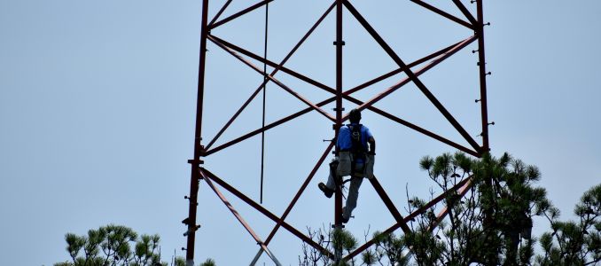 Worker wearing a safety harness climbs a steel tower.