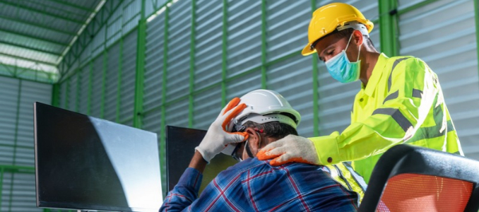 An industrial worker holding his head and neck in pain from a musculoskeletal strain while a safety-clad colleague checks on his neck discomfort.