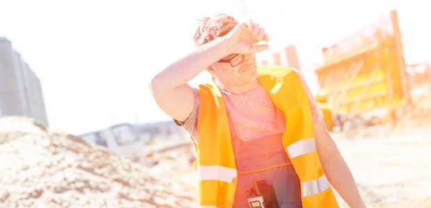 person in orange vest on construction site wiping sweat off brow