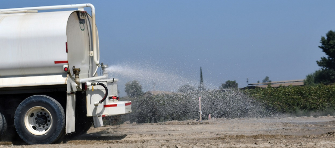 Water truck spraying water onto an unpaved construction site.