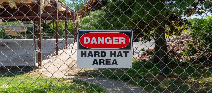 Danger Hard Hat Area sign on a chain link fence, marking a hazardous demolition or construction site