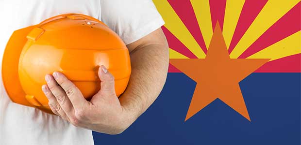 person wearing white shirt holding orange hard hat on left side of photo. Arizona flag (red and yellow lines radiating upward from orange star in middle of flag with bottom half of flag one shade of blue) on right.