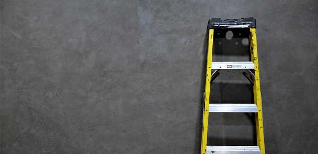 grey chalky wall with yellow-edged ladder leaning against it.