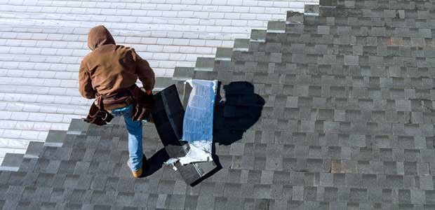 person in brown sweatshirt and blue jeans on roof laying shingles
