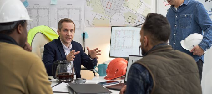 man leading discussion on construction plans and hard hats visible