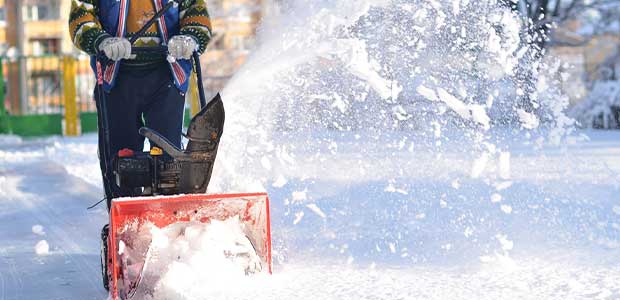 person with grey gloves pushing red snow blower. Snow is coming out of the top of the snow blower to the right of the image