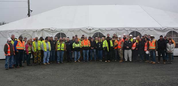 A large group of people stand in front of a white tent.