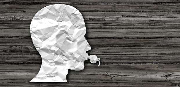 crumpled paper flattened in the shape of a head blowing a whistle against a brown, wood background
