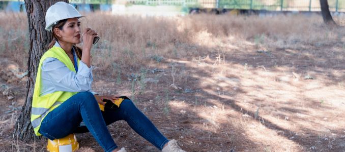 Woman worker with safety vest and hard hat resting under a tree