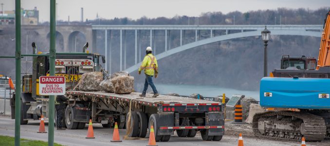Construction worker on back of a semi truck with flatbed trailer loaded with large landscaping boulders