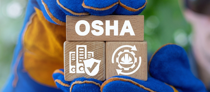 Hands in blue and yellow work gloves holding three wooden blocks that spell out OSHA and display workplace safety icons.