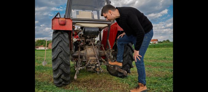 A farmer inspecting the back of a tractor.